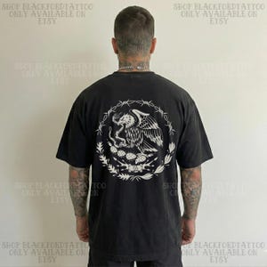 May include: Black t-shirt featuring a white graphic of an eagle, snake, and cactus design within a barbed wire circle. The text "SHOP BLACKFORDTATTOO ONLY AVAILABLE ON ETSY" is printed around the image. The shirt is a dark color.