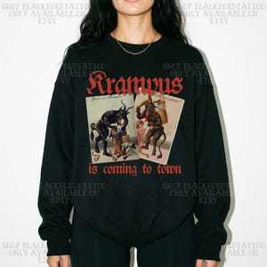 Peut inclure: Un sweat-shirt noir à manches longues avec une impression graphique représentant deux illustrations vintage de Krampus. Le texte rouge au-dessus indique Krampus et le texte rouge en dessous indique is coming to town avec des créatures.
