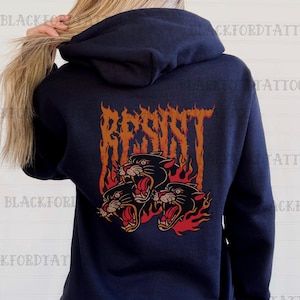 May include: A navy blue hoodie with a graphic of three black panther heads in flames with the word "RESIST" in orange above them.