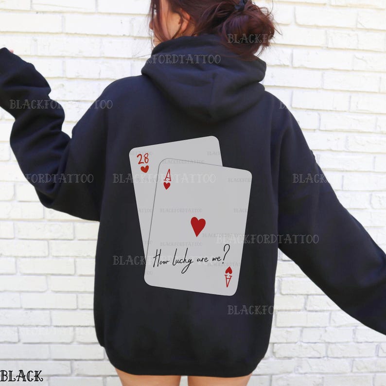 Puede incluir: Sudadera negra con un gr&aacute;fico de dos cartas de juego, un as y un 28, con el texto "How lucky are we?" impreso en las cartas.