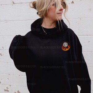 May include: Black hooded sweatshirt with a white 8-ball graphic on fire. The 8-ball is in the center of the chest.