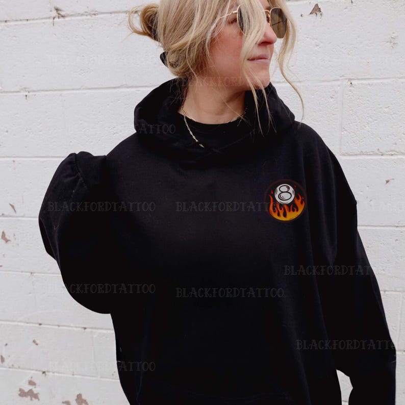May include: Black hooded sweatshirt with a white 8-ball graphic on fire. The 8-ball is in the center of the chest.
