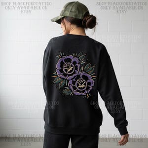 May include: Black sweatshirt featuring a purple rose tattoo design on the back. The roses have a detailed, vintage style with green leaves and a white center. The text "SHOP BLACKFORDTATTOO ONLY AVAILABLE ON ETSY" is printed on the top and bottom.