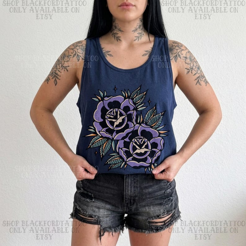 May include: Navy blue tank top featuring a large graphic of two purple roses with green and orange leaves. The text "SHOP BLACKFORDTATTOO ONLY AVAILABLE ON ETSY" is printed on the top and bottom of the image. The tank top is paired with black denim shorts.