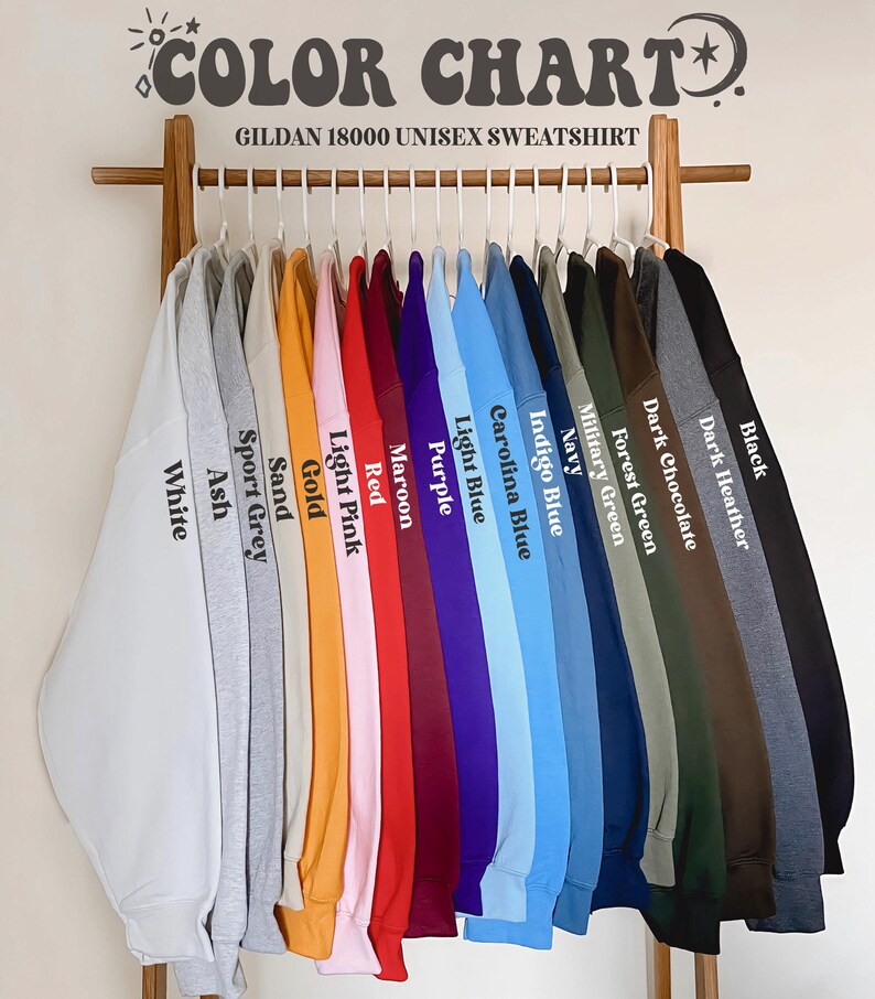 May include: A color chart displaying a variety of Gildan 18000 unisex sweatshirts. The sweatshirts are arranged on a wooden rack, showcasing colors like white, ash, sport grey, sand, gold, light pink, red, maroon, purple, light blue, carolina blue, indigo blue, navy, military green, forest green, dark chocolate, dark heather, and black.