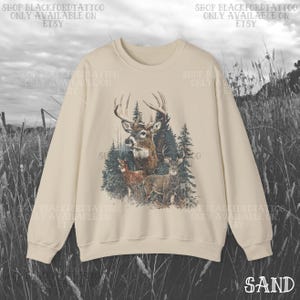 May include: A sand-coloured sweatshirt with a detailed illustration of deer in a forest setting. The graphic includes a buck with large antlers, smaller deer, and evergreen trees. The text "SHOP BLACKFORDTATTOO ONLY AVAILABLE ON ETSY" is printed around the design.
