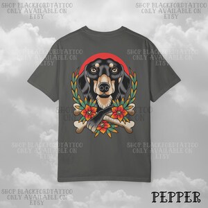 K&ouml;nnte beinhalten: Dunkelgraues T-Shirt mit einem Dackel-Design. Der Hund ist von einem Kranz, Blumen und Knochen umgeben. Der Text "SHOP BLACKFORDTATTOO ONLY AVAILABLE ON ETSY" ist um das T-Shirt gedruckt. Das Wort "PEPPER" ist unten aufgedruckt.
