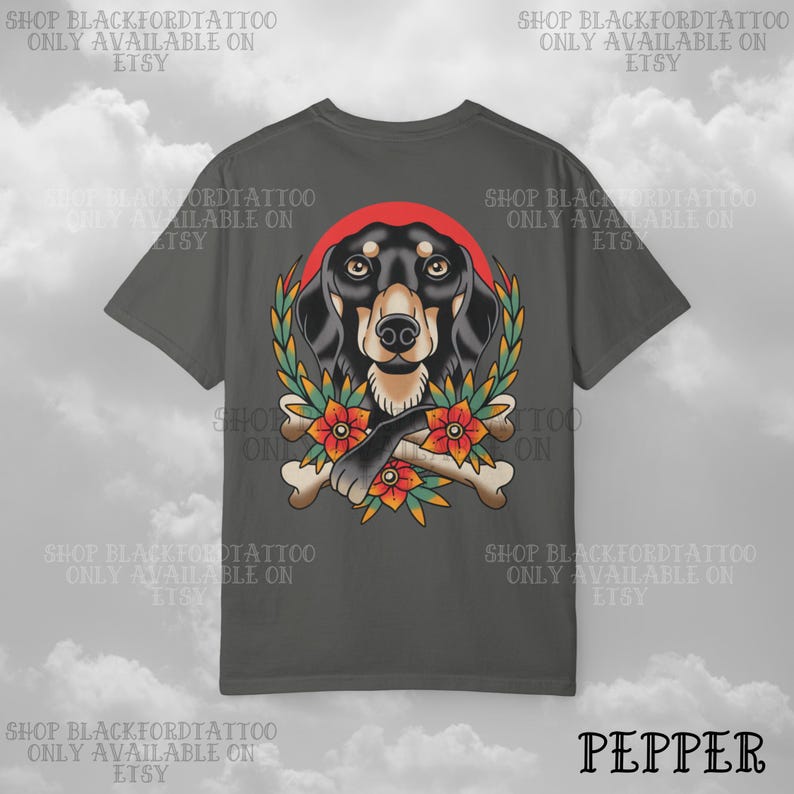 K&ouml;nnte beinhalten: Dunkelgraues T-Shirt mit einem Dackel-Design. Der Hund ist von einem Kranz, Blumen und Knochen umgeben. Der Text "SHOP BLACKFORDTATTOO ONLY AVAILABLE ON ETSY" ist um das T-Shirt gedruckt. Das Wort "PEPPER" ist unten aufgedruckt.