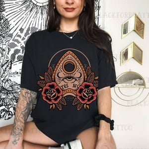 May include: Black t-shirt with a graphic of a Ouija board with the words "YES" and "NO" printed on it. The board is surrounded by red roses.