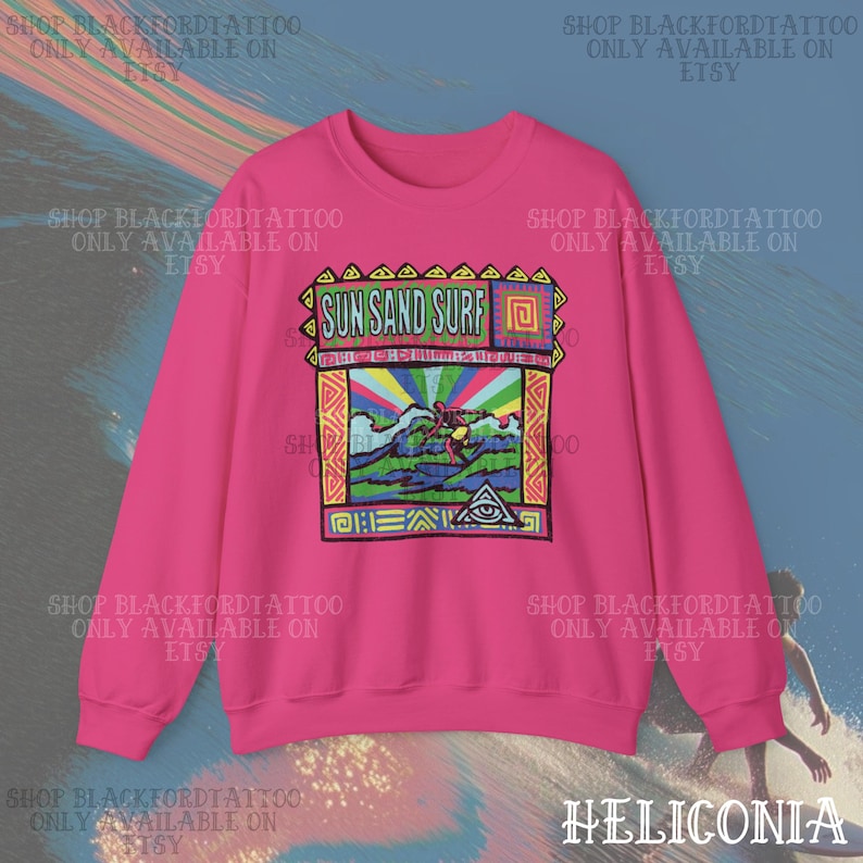 May include: A vibrant pink sweatshirt featuring a colorful graphic with the text "SUN SAND SURF." The design includes a surfer riding a wave, with a rainbow and geometric patterns. The sweatshirt is a crew neck style.