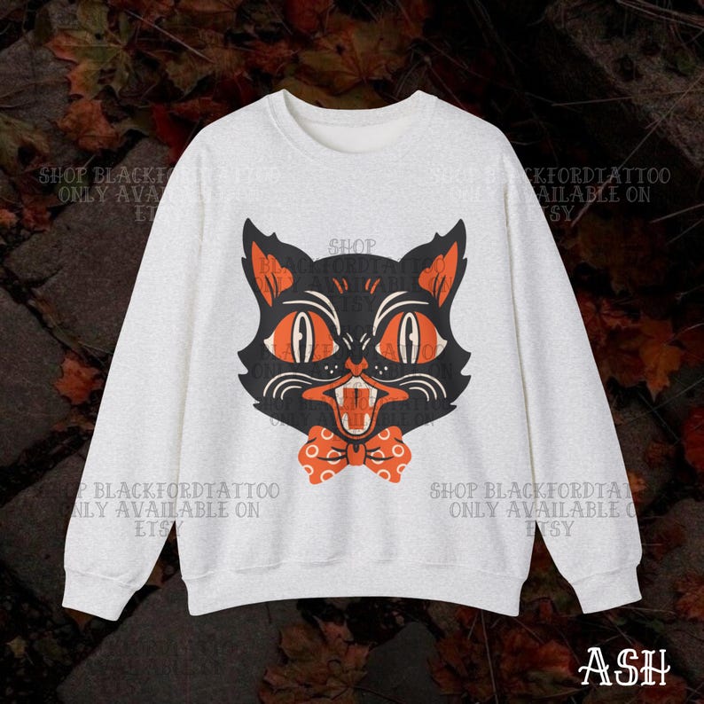 May include: A light gray sweatshirt featuring a vintage-style black cat graphic with orange eyes and a bow tie. The cat's mouth is open, revealing its teeth. Text on the sweatshirt reads "SHOP BLACKFORDTATTOO ONLY AVAILABLE ON ETSY".