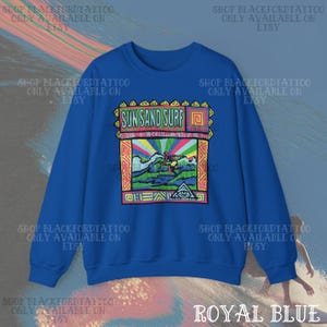 May include: Royal blue sweatshirt with a colorful graphic that reads "Sun Sand Surf." The graphic features a surfer, waves, and a rainbow. The sweatshirt is a crew neck style.