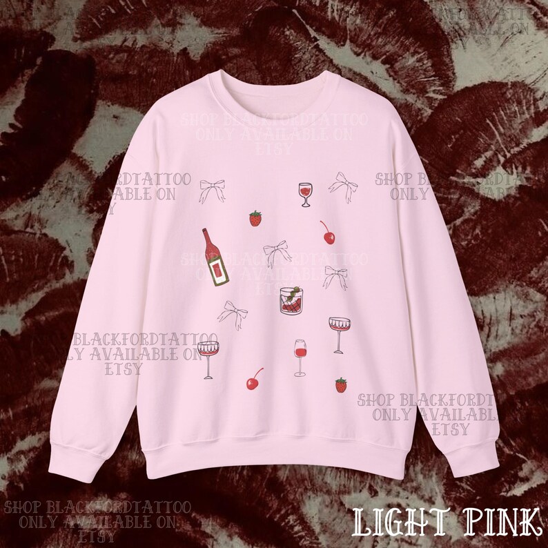 May include: Light pink sweatshirt with a scattered pattern of wine glasses, bows, cherries, strawberries, and a wine bottle. The text "SHOP BLACKFORDTATTOO ONLY AVAILABLE ON ETSY" is printed around the design. The bottom right corner reads "LIGHT PINK".