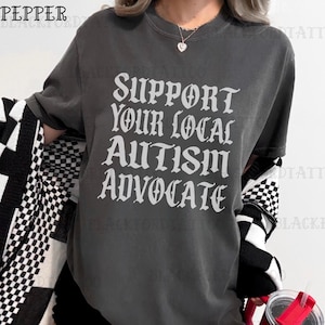 May include: A gray t-shirt with the text "Support Your Local Autism Advocate" printed in a white gothic font.