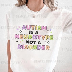 May include: White t-shirt with the text "AUTISM IS A NEUROTYPE NOT A DISORDER" in colorful letters. The text is surrounded by small stars and hearts.