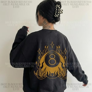 May include: Black sweatshirt with a gold graphic of an eight ball surrounded by flames and stars. The text "SHOP BLACKFORDTATTOO ONLY AVAILABLE ON ETSY" is printed around the image.