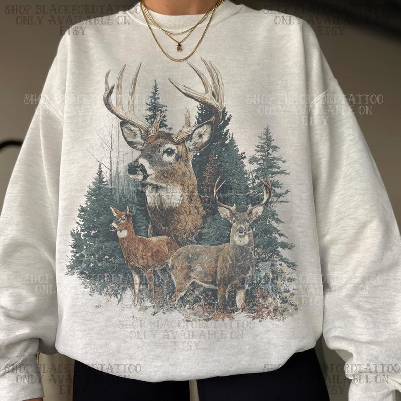 May include: A pale grey sweatshirt with a detailed illustration of three deer in a forest setting. The design includes a large buck with prominent antlers, two smaller deer, and evergreen trees. The text "SHOP BLACKFORDTATTOO ONLY AVAILABLE ON ETSY" is printed on the sweatshirt.