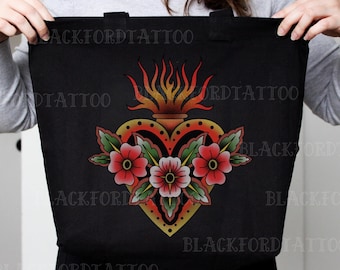 Op de afbeelding: Zwarte draagtas met een hartvormig ontwerp, vlammen en bloemen. Het hart is geel met rode en oranje accenten, en de bloemen zijn rood met groene bladeren. De tas heeft twee zwarte handvatten.