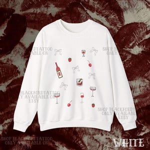 May include: White sweatshirt with a scattered pattern of wine glasses, bows, cherries, strawberries, and a wine bottle. The text "WHITE" is at the bottom right. The words "BLACKFORDTATTOO ONLY AVAILABLE ON ETSY" are printed on the sweatshirt.
