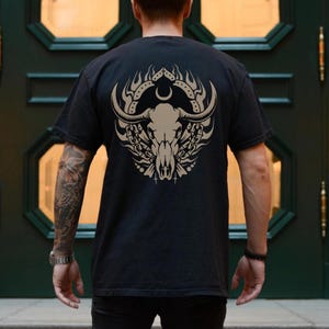 Puede incluir: Una camiseta negra con un estampado gr&aacute;fico de un cr&aacute;neo de toro con llamas y cadenas. El cr&aacute;neo est&aacute; rodeado por un c&iacute;rculo con una luna creciente y estrellas.
