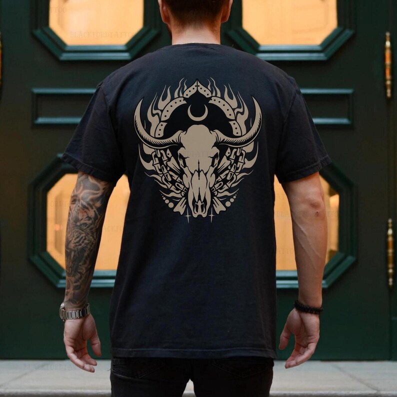 Puede incluir: Una camiseta negra con un estampado gr&aacute;fico de un cr&aacute;neo de toro con llamas y cadenas. El cr&aacute;neo est&aacute; rodeado por un c&iacute;rculo con una luna creciente y estrellas.