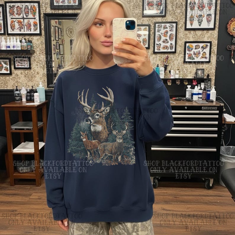 May include: A navy blue sweatshirt with a detailed graphic of deer in a forest. The design includes a buck with large antlers and two smaller deer. The text "SHOP BLACKFORDTATTOO ONLY AVAILABLE ON ETSY" is printed on the sweatshirt.