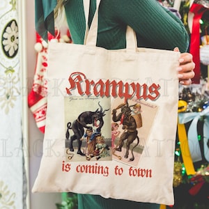May include: A white canvas tote bag with the words "Krampus is coming to town" printed in red. The bag features two vintage illustrations of Krampus, a horned, demonic figure associated with Christmas folklore.