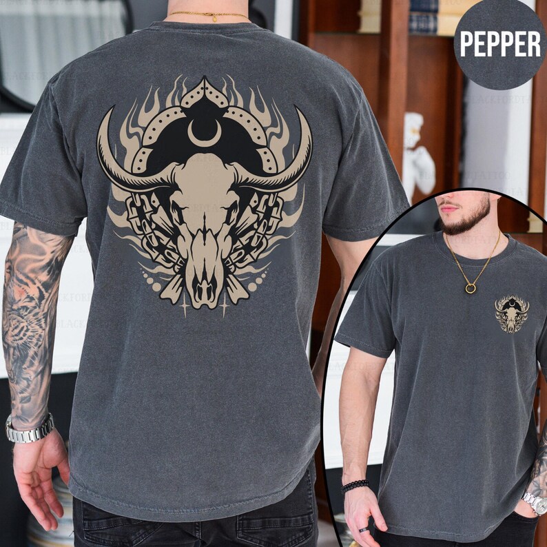 Puede incluir: Una camiseta gris oscuro con un estampado gr&aacute;fico de un cr&aacute;neo de toro con cuernos y cadenas. El cr&aacute;neo est&aacute; rodeado de llamas y una luna creciente. La palabra "Pepper" est&aacute; impresa en blanco en el lado derecho de la imagen.