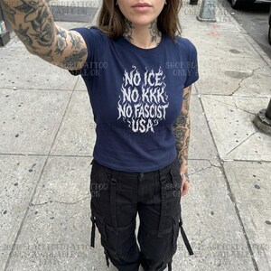 May include: Navy blue t-shirt with the text "NO ICE NO KKK NO FASCIST USA" in white. The shirt is short-sleeved and has a crew neck. The person is wearing black cargo pants.