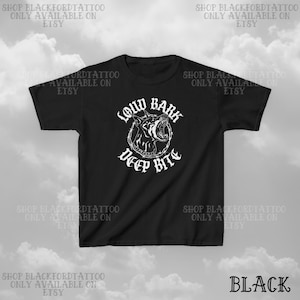 Puede incluir: Camiseta negra con un dise&ntilde;o gr&aacute;fico blanco de una cabeza de perro gru&ntilde;endo dentro de un c&iacute;rculo de alambre de p&uacute;as. El texto "LOUD BARK DEEP BITE" est&aacute; encima y debajo del gr&aacute;fico. La palabra "BLACK" est&aacute; en la esquina inferior derecha.