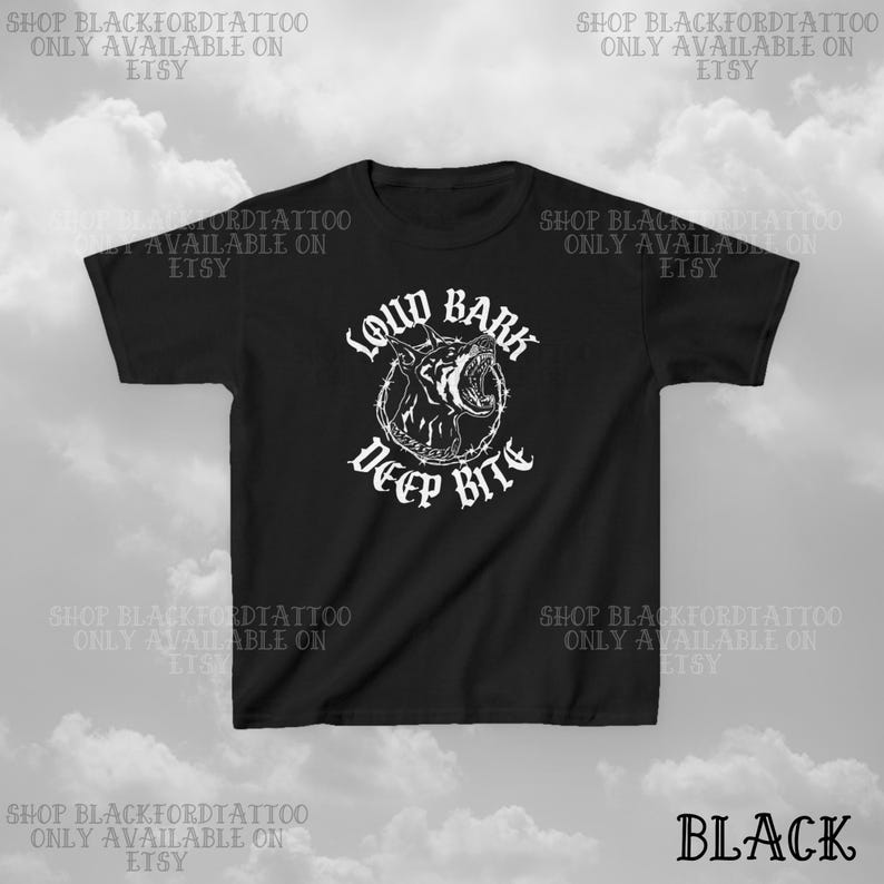 Puede incluir: Camiseta negra con un dise&ntilde;o gr&aacute;fico blanco de una cabeza de perro gru&ntilde;endo dentro de un c&iacute;rculo de alambre de p&uacute;as. El texto "LOUD BARK DEEP BITE" est&aacute; encima y debajo del gr&aacute;fico. La palabra "BLACK" est&aacute; en la esquina inferior derecha.