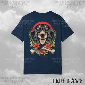 K&ouml;nnte beinhalten: Marineblaues T-Shirt mit einer detaillierten Illustration eines Dackelhundes, einem roten Heiligenschein, einem Lorbeerkranz, Blumen und gekreuzten Knochen. Der Text "SHOP BLACKFORDTATTOO ONLY AVAILABLE ON ETSY" ist um das T-Shirt gedruckt. Der Text "TRUE NAVY" ist unten gedruckt.