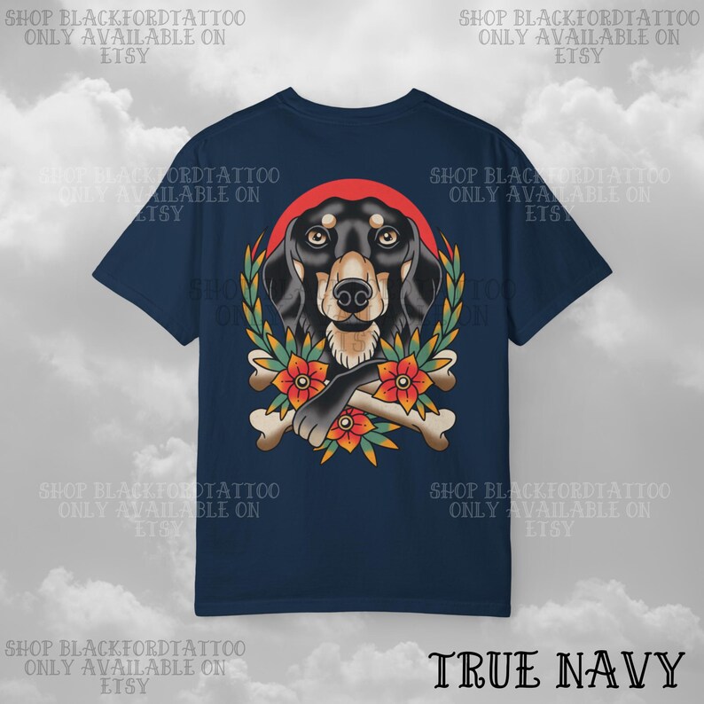 K&ouml;nnte beinhalten: Marineblaues T-Shirt mit einer detaillierten Illustration eines Dackelhundes, einem roten Heiligenschein, einem Lorbeerkranz, Blumen und gekreuzten Knochen. Der Text "SHOP BLACKFORDTATTOO ONLY AVAILABLE ON ETSY" ist um das T-Shirt gedruckt. Der Text "TRUE NAVY" ist unten gedruckt.