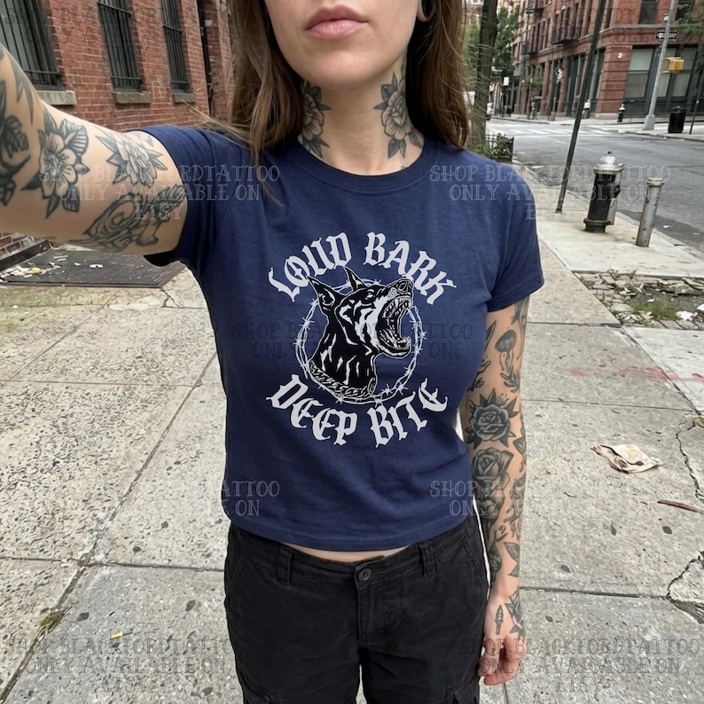 Puede incluir: Camiseta azul marino con el texto "LOUD BARK DEEP BITE" y un gr&aacute;fico de un perro gru&ntilde;endo dentro de un c&iacute;rculo de alambre de p&uacute;as. La camiseta es de estilo ajustado.