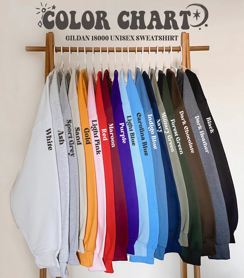 May include: A colour chart of Gildan 18000 unisex sweatshirts. The sweatshirts are displayed on a wooden rack, showcasing a variety of colours including white, ash, sport grey, sand, gold, light pink, red, maroon, purple, light blue, carolina blue, indigo blue, navy, military green, forest green, dark chocolate, dark heather, and black.