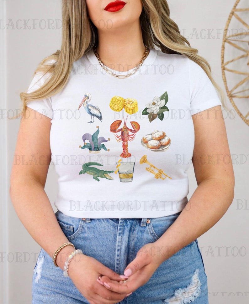 May include: White t-shirt with a colorful illustration of various symbols associated with Mardi Gras, including a pelican, a fleur-de-lis, a crawfish, a glass of Hurricanes, and beignets.