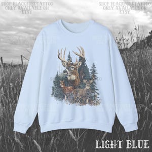 May include: Pale blue sweatshirt with a detailed graphic of deer in a forest. The design includes several deer, trees, and foliage. The text "SHOP BLACKFORDTATTOO ONLY AVAILABLE ON ETSY" is printed at the top. The words "LIGHT BLUE" are printed at the bottom.
