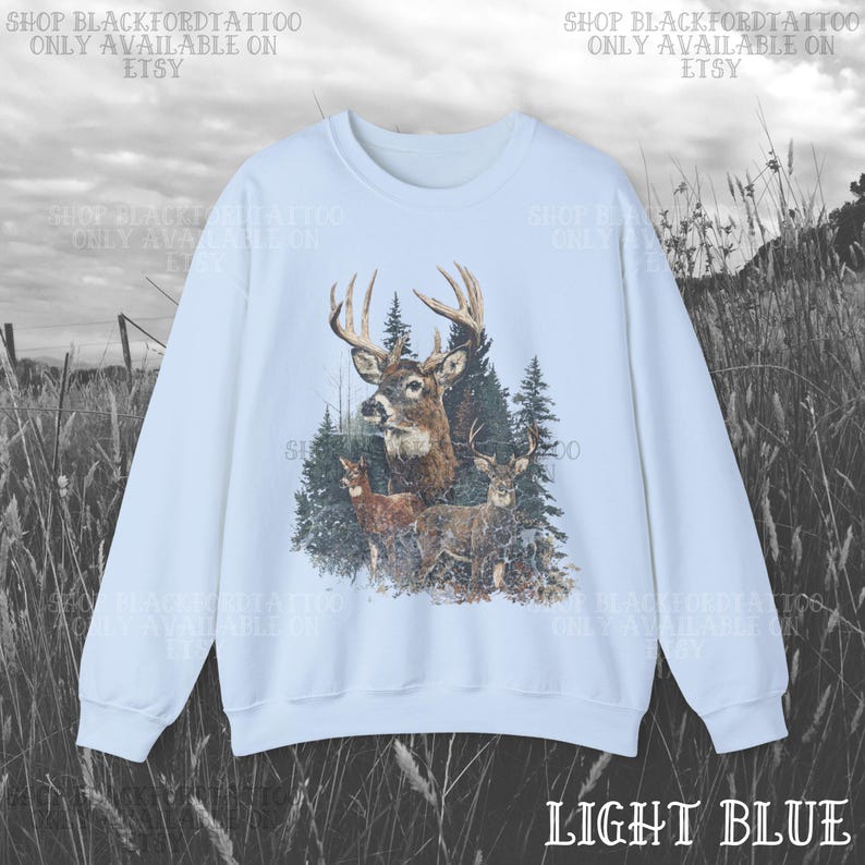May include: Pale blue sweatshirt with a detailed graphic of deer in a forest. The design includes several deer, trees, and foliage. The text "SHOP BLACKFORDTATTOO ONLY AVAILABLE ON ETSY" is printed at the top. The words "LIGHT BLUE" are printed at the bottom.