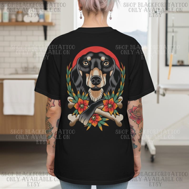 K&ouml;nnte beinhalten: Schwarzes T-Shirt mit einer Tattoo-Illustration eines Dackelhundes. Das Design umfasst einen roten Heiligenschein, florale Elemente und gekreuzte Knochen. Der Text "SHOP BLACKFORDTATTOO ONLY AVAILABLE ON ETSY" ist um das Shirt gedruckt.
