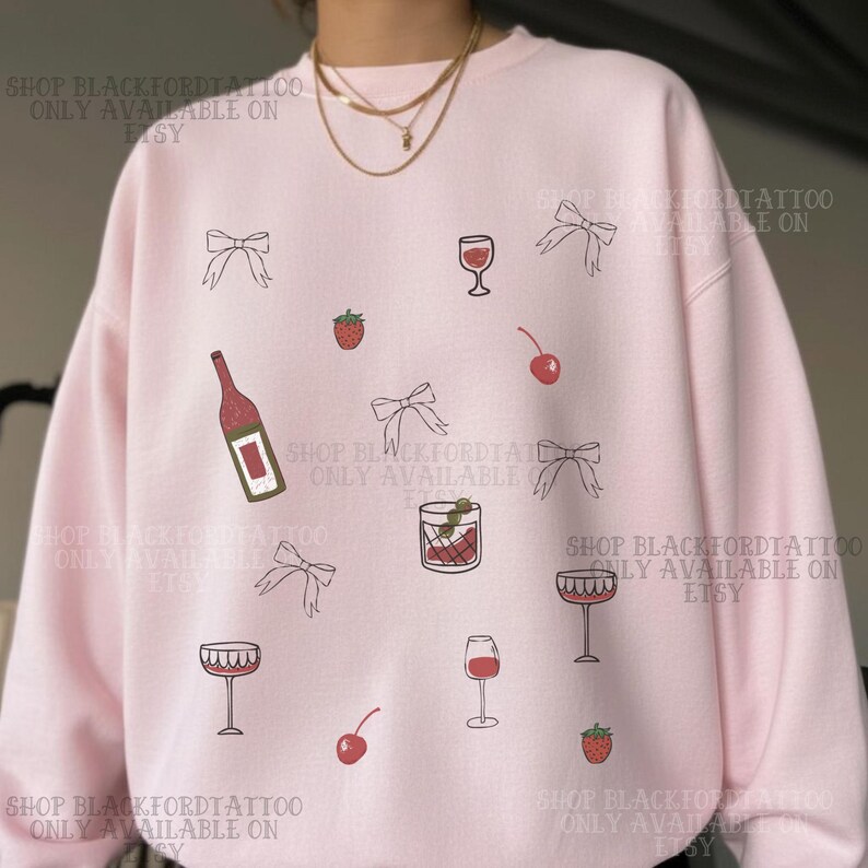 May include: Pink sweatshirt with a repeating pattern of wine glasses, bows, cherries, strawberries, and a wine bottle. The text "SHOP BLACKFORDTATTOO ONLY AVAILABLE ON ETSY" is printed around the edges of the sweatshirt.