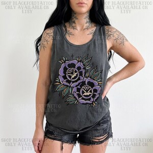 May include: Dark gray tank top featuring a floral design of two purple roses with green leaves and yellow accents. The text "SHOP BLACKFORDTATTOO ONLY AVAILABLE ON ETSY" is printed on the top. The tank top is worn with black shorts.