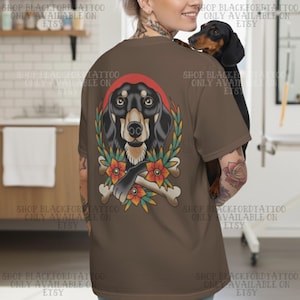 K&ouml;nnte beinhalten: Braunes T-Shirt mit einer Tattoo-Illustration eines Dackelhundes mit rotem Bandana, umgeben von Lorbeerkranz, Blumen und gekreuzten Knochen. Der Text "SHOP BLACKFORDTATTOO ONLY AVAILABLE ON ETSY" ist auf dem Shirt aufgedruckt.