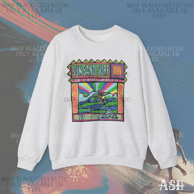 May include: A light gray sweatshirt with a colorful graphic that says "SUN SAND SURF". The graphic features a surfer, waves, and a rainbow. The sweatshirt has long sleeves and a crew neck.