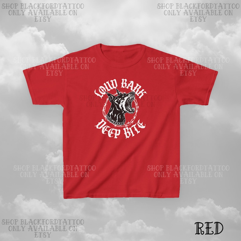 Puede incluir: Camiseta roja con un gr&aacute;fico en blanco y negro de un Doberman Pinscher y las palabras "Loud Bark Deep Bite" en letras g&oacute;ticas blancas. La camiseta tiene mangas cortas y cuello redondo.