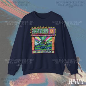 May include: Navy blue sweatshirt with a colorful graphic that reads "Sun Sand Surf." The graphic features a surfer riding a wave with a rainbow background. The sweatshirt has a crew neck and long sleeves.