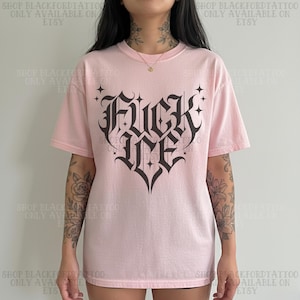 May include: A light pink t-shirt with the words "FUCK ME" in a gothic font, designed in a heart shape. The shirt has short sleeves and a crew neck. The text "SHOP BLACKFORDTATTOO ONLY AVAILABLE ON ETSY" is printed on the top and bottom of the image.