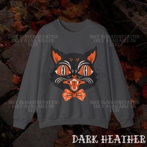 May include: Dark heather gray sweatshirt featuring a vintage-style black cat graphic with orange eyes, ears, and a bow tie. The text "DARK HEATHER" is at the bottom. The sweatshirt has the text "SHOP BLACKFORDTATTOO ONLY AVAILABLE ON ETSY" repeated around the image.