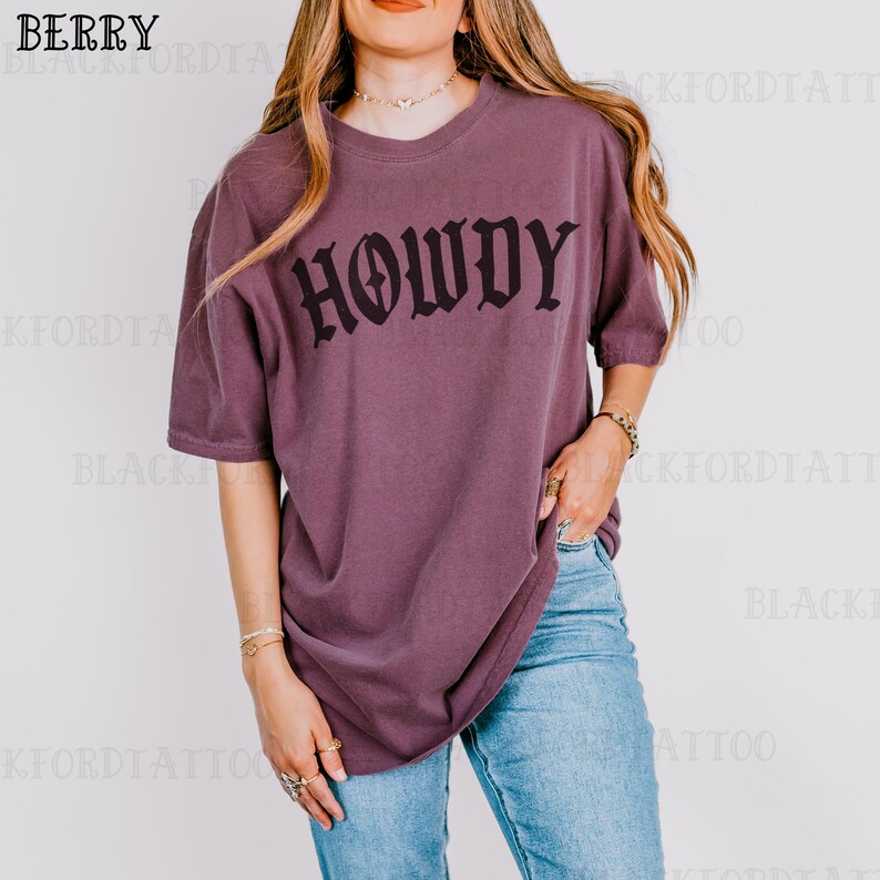 May include: A purple oversized t-shirt with the word "Howdy" printed in black gothic lettering.