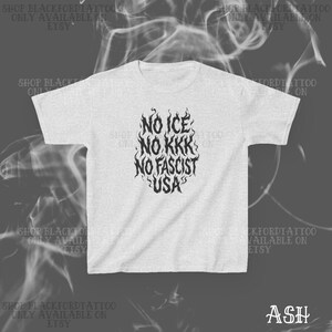 May include: Ash-colored t-shirt with a black graphic. The graphic reads "NO ICE, NO KKK, NO FASCIST, USA" in a stylized flame design. The shirt is a crew neck style.