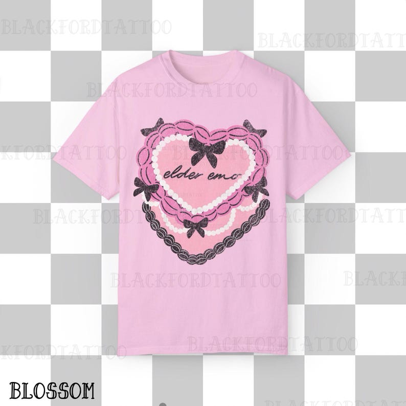 May include: A light pink t-shirt featuring a heart-shaped design with the words "elder emo" in the center. The heart is decorated with black bows, a pearl-like border, and a black lace trim. The word "BLOSSOM" is at the bottom.